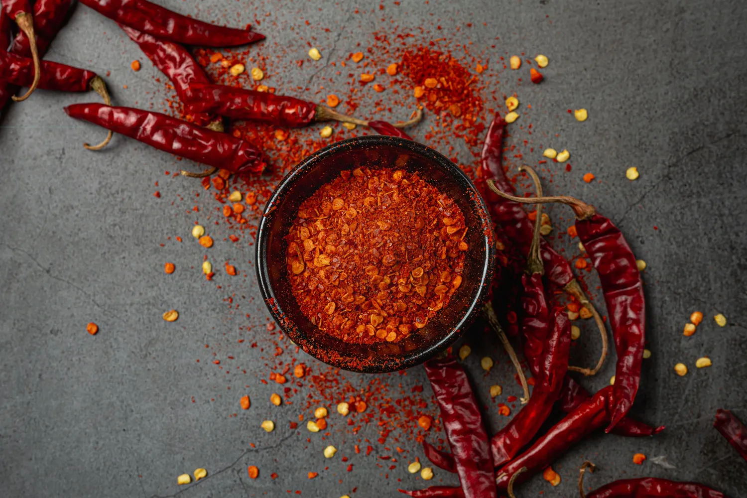 Chili flakes in a bowl, whole dried chilies scattered around it